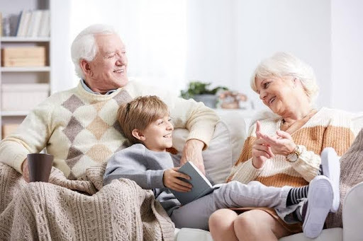 Grandparents sharing stories with a smiling child on a sofa, reflecting family bonds and value-based upbringing at JMIS.